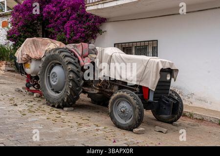 À Sirince, un tracteur rouge est garé à côté d'une maison blanche avec des bougainvilliers violets, symbolisant le mode de vie agricole rural des villages turcs. Banque D'Images