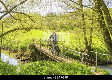 Un cycliste traverse un petit pont sur une rivière, entouré de verdure printanière, Gechingen, district de Calw, Allemagne, Europe Banque D'Images