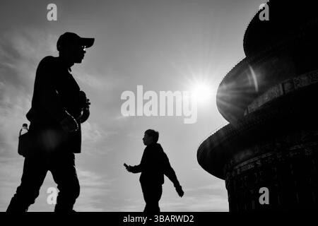 Deux personnes en silhouette se croisent devant le Temple du ciel, capturées dans un moment de mouvement et d’énergie urbaine. Banque D'Images