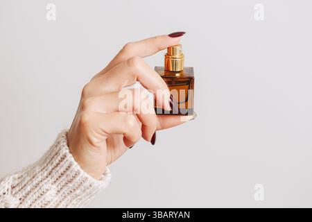 Main de femme tenant bouteille de parfum. Récipient pulvérisateur en verre brun. Produit de beauté sur fond blanc. Concept cosmétique minimal élégant de soin de la peau. Banque D'Images