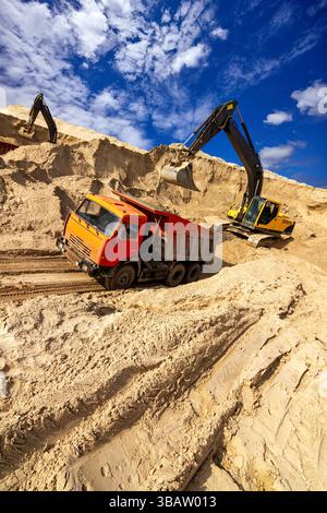 La pelle jaune charge du sable dans un camion à benne basculante dans une carrière de construction sous un ciel bleu vif Banque D'Images