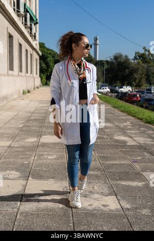 Jeune femme médecin marchant près de l'hôpital portant un manteau blanc et un stéthoscope Banque D'Images