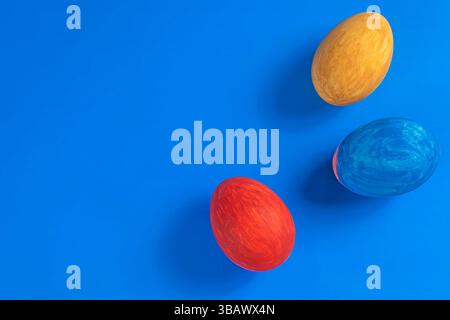 Trois œufs de Pâques colorés en rouge, jaune et bleu sont placés sur un fond bleu vif, un design minimaliste idéal pour la célébration ou la saison pr Banque D'Images