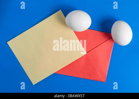 Un arrangement vibrant avec des œufs blancs, une feuille de papier jaune et une enveloppe rouge sur une surface bleu vif. Parfait pour les vacances, Pâques ou la communication Banque D'Images