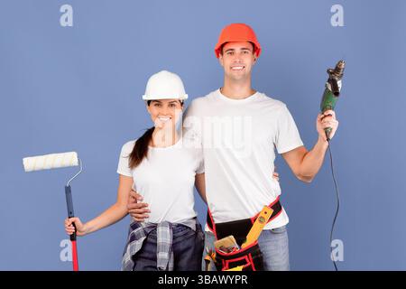 Rénovation de la maison. Couple souriant avec perceuse et pinceau à rouleaux dans les mains Banque D'Images