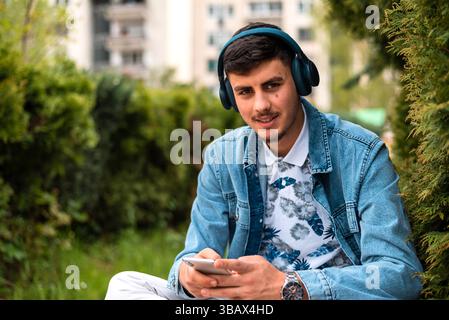 Un jeune homme heureux avec des écouteurs utilisant un téléphone portable à l'extérieur. Banque D'Images