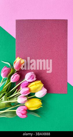 Bouquet de tulipes roses, jaunes et oranges placé sur un fond géométrique rose et vert. Un carton rouge texturé est positionné au centre, creati Banque D'Images