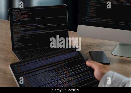 Un programmeur de site Web travaillant avec plusieurs écrans affichant le code et les données, un cadre de bureau moderne, montrant l'accent et l'activité technique Banque D'Images