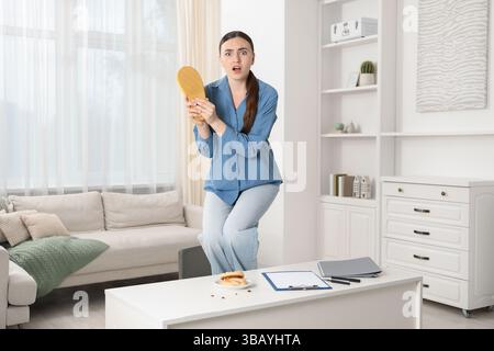 Jeune femme avec pantoufle regardant dans le dégoût des cafards sur la table blanche à l'intérieur. Problème de ravageur Banque D'Images