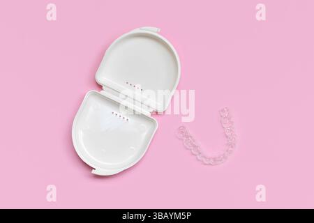 Vue de dessus des aligners transparents personnalisés de garde de morsure de dents dentaires pour mâchoire inférieure avec étui de rangement blanc sur fond rose Banque D'Images