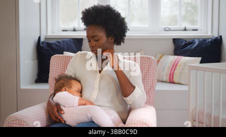 Nouvelle mère souffrant de dépression post-natale tenant la fille de bébé endormi dans la pépinière à la maison Banque D'Images