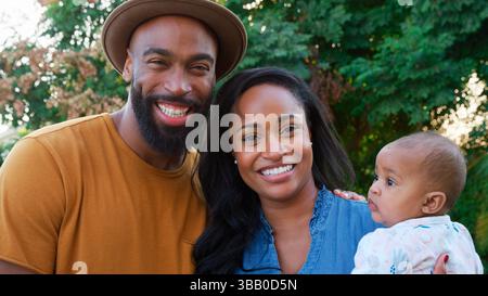 Sourire afro-américain Cuddling et jouer avec bébé fille dans Garden at Home Banque D'Images