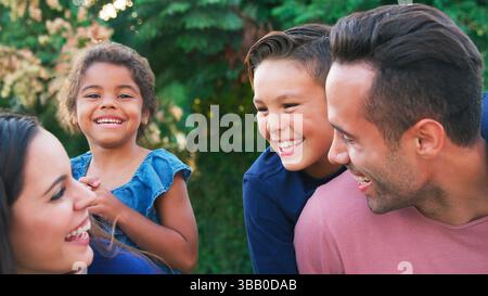 Portrait d'une famille hispanique souriante avec des parents donnant des enfants Piggyback Promenades dans le jardin à la maison Banque D'Images