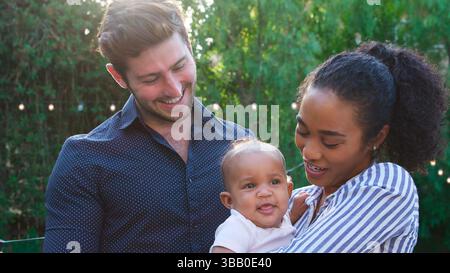 Parents affectueux tenant bébé fille à la maison à l'extérieur dans le jardin Banque D'Images