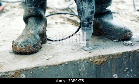 Gros plan de forage dans le béton sur un chantier de construction. Un gros plan détaillé d'un travailleur de la construction botte et perce alors qu'il perce dans un béton Banque D'Images