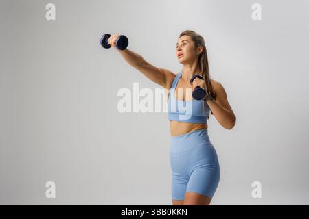 Femme exerçant avec des haltères à l'intérieur pendant une routine de fitness dans des vêtements d'action bleu clair Banque D'Images