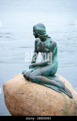 Une statue en bronze d'une sirène se trouve sur un rocher au bord de l'eau à Copenhague. Ce monument emblématique attire les visiteurs qui admirent sa beauté et capturent des souvenirs avec son art unique. Banque D'Images