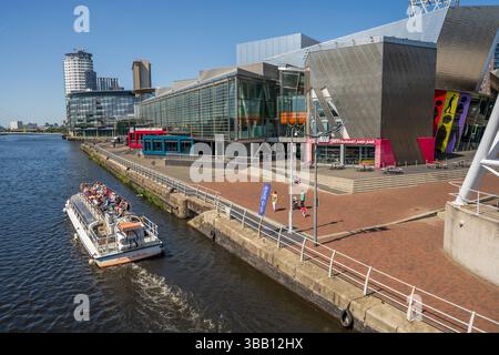Un bateau de plaisance passe devant le centre de Lowry sur Salford Quays. L'ancien Pomona accoste à l'extrémité de Manchester du canal des navires de Manchester. Banque D'Images