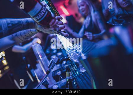 Rome, italie 4 mai 2025 : barman avec les bras tatoués versant de la liqueur rouge d'une bouteille dans des verres à dose sur un comptoir de bar dans une boîte de nuit, avec flou Banque D'Images