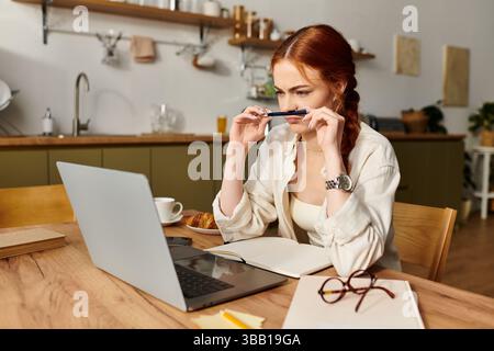 Une femme aux cheveux rouges profondément dans la pensée, entourée d'une atmosphère de cuisine chaleureuse et accueillante. Banque D'Images
