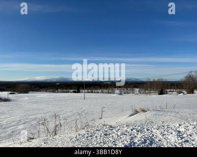 Une belle scène hivernale, mettant en valeur des champs enneigés, des montagnes et un ciel bleu clair. Banque D'Images