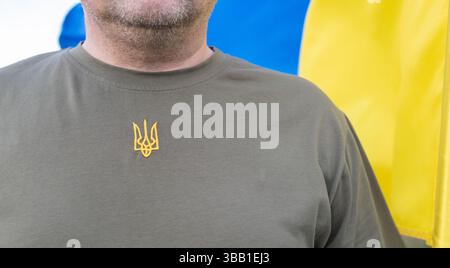 Homme ukrainien méconnaissable portant un T-shirt kaki avec un trident brodé dessus et un drapeau jaune et bleu de l'état de l'Ukraine. gros plan, co Banque D'Images