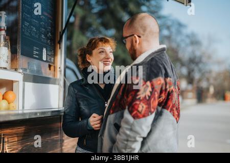Couple souriant profitant de la conversation à l'extérieur près d'un stand de nourriture Banque D'Images