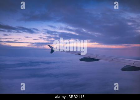 Avion volant au-dessus des nuages colorés du ciel pendant le coucher du soleil ou le lever du soleil paysage nuageux, vue depuis la fenêtre de l'avion des éoliennes et de l'horizon Banque D'Images