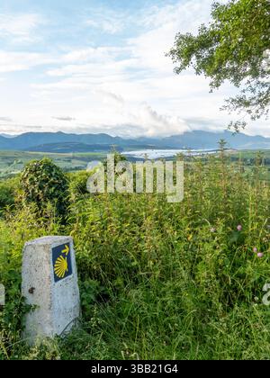 Jalon concret indiquant la voie à suivre pour les pèlerins marchant le Camino de santiago, avec un beau paysage en arrière-plan pendant un ensoleillé Banque D'Images