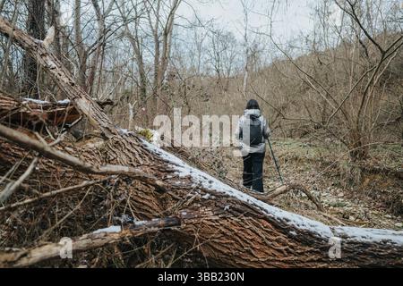 Randonneur explorant un chemin forestier d'hiver au milieu de la neige et des arbres tombés au cours d'une aventure en plein air Banque D'Images