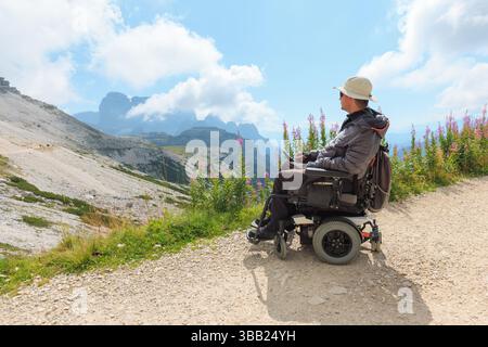 Homme handicapé en fauteuil roulant explore les belles Dolomites en Italie. Il apprécie le paysage pittoresque entouré de montagnes et dynamique Banque D'Images