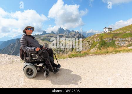 Un homme handicapé utilisant un fauteuil roulant explore les Dolomites à couper le souffle en Italie par une journée ensoleillée. Il regarde un paysage de montagne magnifique pendant Banque D'Images
