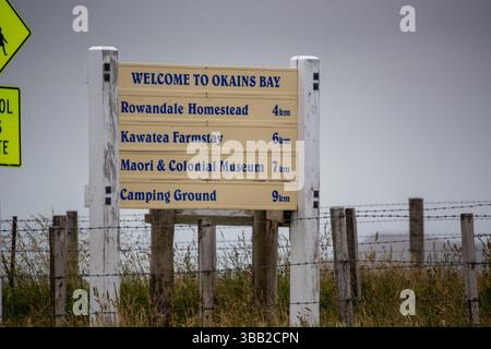 Un panneau accueillant les visiteurs à Okains Bay, indiquant les distances vers diverses attractions locales, y compris Rowandale Homestead, Kawatea Farmstay, Maori & Co Banque D'Images
