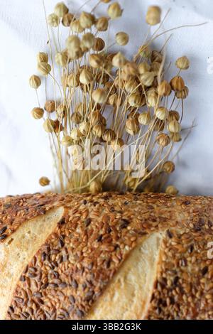 Pain saupoudré de graines de lin et de sésame sur une nappe de lin blanc. Gousses de graines de lin. Pain au levain. Banque D'Images
