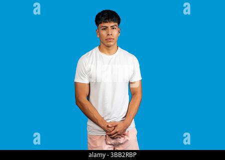 Portrait d'un jeune homme latino sérieux debout avec les mains pliées sur un fond bleu vif Banque D'Images