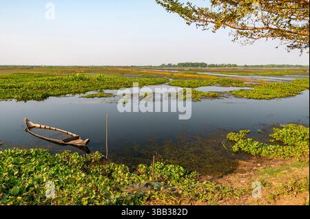 Un petit bateau ancien style khmer, partiellement submergé dans les eaux peu profondes du lac, est assis dans la lumière du soleil de l'après-midi, surplombant de beaux paysages de lac plat. Banque D'Images