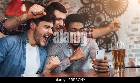 Divers fans de football regardant le football sur smartphoner dans un pub Banque D'Images