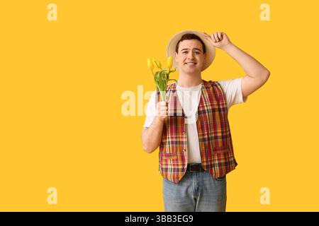 Jeune homme en chapeau avec des fleurs de tulipe sur fond jaune Banque D'Images