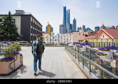 Vue large d'un touriste traversant un pont à Pudong, Shanghai, avec des fleurs en fleurs et l'horizon avec Shanghai Tower et SWFC. Banque D'Images