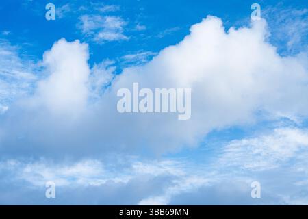 Des nuages blancs moelleux dérivent à travers un ciel bleu clair dans ce paisible paysage nuageux, évoquant un sentiment de calme et d'émerveillement. Banque D'Images