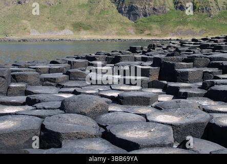 Colonnes hexagonales sombres vues d'en haut avec de l'eau et une falaise en arrière-plan à Giant's Causeway en Irlande du Nord Banque D'Images