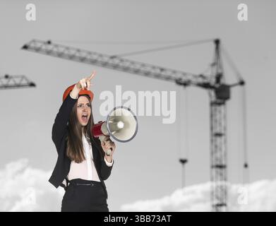 Jeune femme builder in hardhat crier dans un mégaphone Banque D'Images