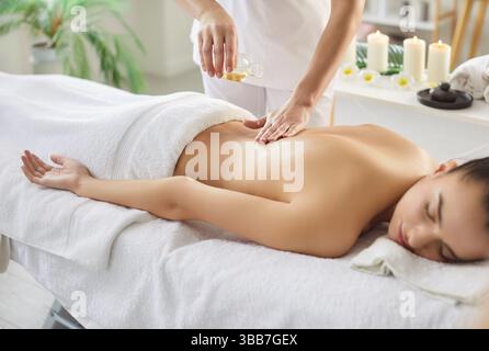Thérapeute appliquant l'huile de massage sur le dos des femmes qui est allongé sur la table de massage au spa Banque D'Images