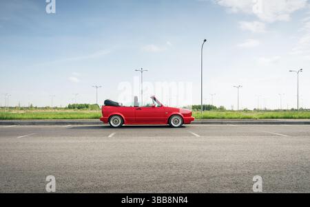 Vue de profil latérale du cabriolet Volkswagen Golf classique. Rouge VW golf mk1 dans un grand parking vide à la campagne, ciel propre en arrière-plan. Banque D'Images