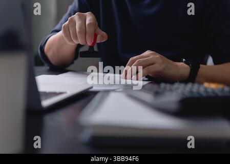 Un professionnel de l'entreprise estampillant un document officiel dans un environnement de bureau, symbolisant l'approbation des documents et les processus de paperasse commerciale. Banque D'Images