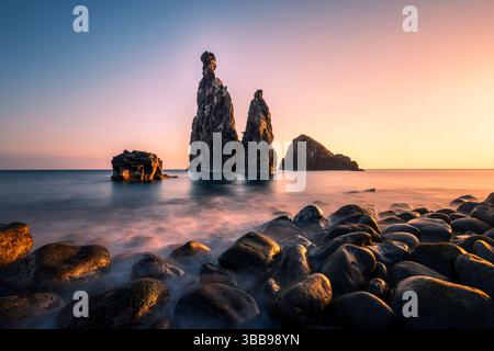 Sunset projette une lueur dorée sur les formations rocheuses côtières emblématiques de Madère, capturées dans une image tranquille à longue exposition qui met en évidence l'interaction de Li Banque D'Images