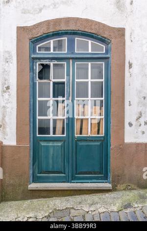 Porte sarcelle patinée avec verre brisé et planches en bois. Gros plan d'une double porte sarcelle vieillie avec des vitres brisées partiellement recouvertes par un plan en bois Banque D'Images