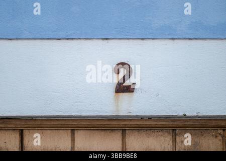Rouillé numéro deux sur le mur texturé. Gros plan d'une maison en métal rouillé et altéré numéro « 2 » apposée sur un mur blanc texturé avec une section supérieure bleu clair Banque D'Images