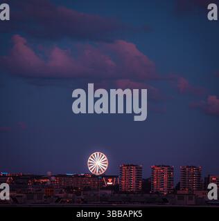 Gratte-ciel crépusculaire d'une ville moderne avec une grande roue brillante et des immeubles de grande hauteur sous un ciel nocturne spectaculaire. Banque D'Images