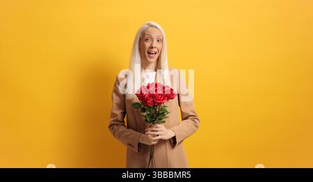 Femme tenant des roses rouges sur un fond jaune Banque D'Images